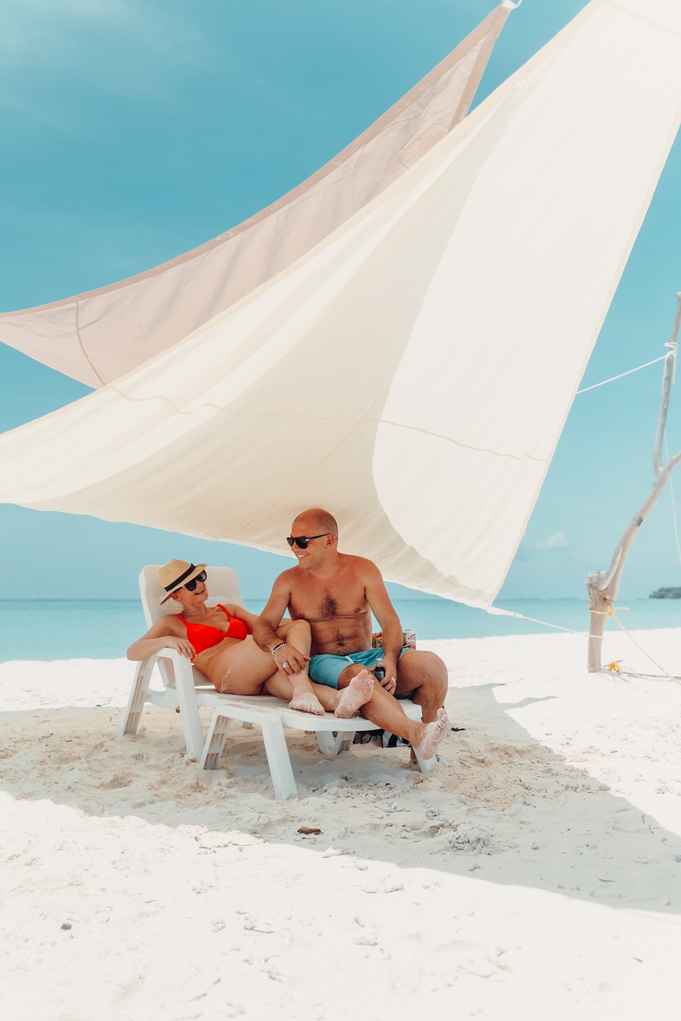 Guests relaxing together beneath a sail shade on a white sandbank
